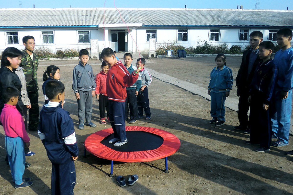 A boy jumps on a trampoline and is surrounded by kids of various age.